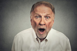 Portrait of a shocked stunned senior man with wide open mouth isolated on gray wall background